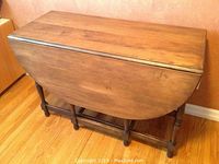 Gateleg table in folded state showing wooden panel leaves and turned legs.