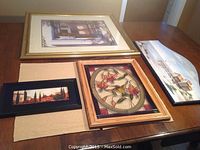 Five framed art pieces on table showing variety of sizes and scenes including stained glass and painted wood.