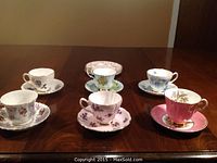 Six tea cups with six matching saucers, each featuring different floral designs and gold rims, arranged on wooden table
