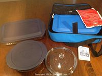 Two Pyrex glass casserole dishes with gray plastic lids and a clear glass lid. Also shown is a blue carry bag used once.