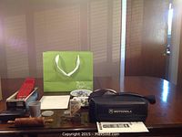 Vintage collectibles displayed on a wooden table including a Motorola mobile phone with carrying case, Merlin handheld game, and Sony Walkman along with other items.