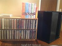 Photo of wooden CD rack with two rows of CDs and five Gilmore Girls DVD box sets stacked on top; black CD carousel beside the rack.
