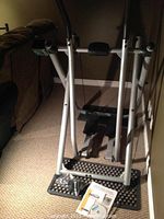 Front view of the elliptical machine showing foot pedals, padded handles, and instruction manual on the floor.