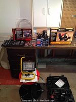 Overview of work light, sabre saw box, socket set tray, drill case, brad nailer box and stool on bench