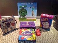 Clay sculpting kit, unopened game boxes of Balderdash, Cranium, and Taboo, dart links game box, and red pouch with marbles.
