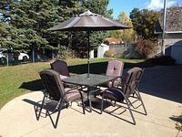 Full set of patio table with glass top, umbrella, and four chairs with cushions arranged on patio.