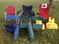 Photo showing four folding chairs, two yellow life jackets, and a green carrying bag for a small tent placed on grass.
