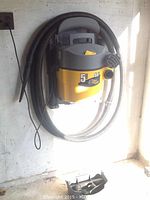 Dirt Hound 5 gallon wet dry vacuum mounted on wall with hose wrapped around unit, accessories below.