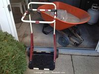 Orange double wheel wheelbarrow and maroon yard cart with lid in background