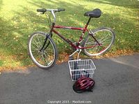 Right side view of men's red 18 inch mountain bike with front basket and helmet on ground nearby
