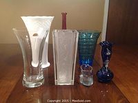 Group shot showing six vases: large white painted vintage vase with chip, rectangular frosted etched vase, small clear vase, tall red vase, turquoise blue textured vase and navy blue floral vase