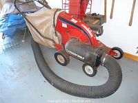 Side view of chipper/vac unit showing red metal housing, hose and full canvas bag