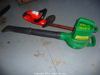 Black & Decker red and black electric hedge trimmer next to Weed Eater green blower/vac on floor.