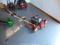 Photo showing the full side view of the Toro lawnmower with a silver handlebar and red deck on a blue floor.