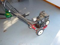 Front side view showing metal frame, engine, handlebar, and front wheels of the edger.