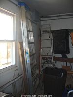 Three ladders of different sizes against a wall, including an extension ladder (left) and two step ladders. The extension ladder features multiple sections with blue rung locks.