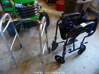 Photo showing silver two-wheeled walker and blue Roscoe transport wheelchair close together on a concrete floor with other items in background.