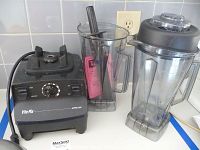 Vita-Mix motor base with wet and dry containers, lid and tamper on countertop