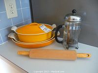 Photo showing three stacked yellow enameled cast iron cookware pieces and a wooden rolling pin on a kitchen counter near an electrical outlet.