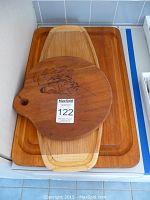 Three wooden cutting boards stacked; round board with floral engraving on top, rectangular bamboo board in middle, largest rectangular board with groove at bottom.