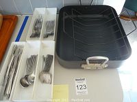 Roasting pan beside tray with organized Oneida flatware including knives, spoons, and forks