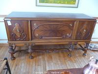 Front view of solid wood buffet showing carved designs, brass round knobs, and turned legs with curved supports on hardwood floor.