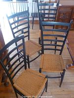 Four ladder-back chairs with black frames and woven natural fiber seats grouped together on a wood floor.