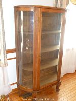 Full-height front view of oak curio cabinet showing curved glass door, wooden frame and three interior shelves.