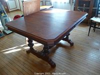 Full view of solid wood dining table with ornate turned legs and leaf extension in extended position.