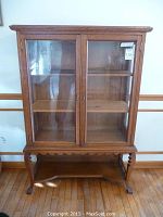 Front view of oak curio cabinet with two glass doors, carved apron, lower shelf and straight legs