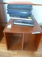 Teak rolling record cabinet with 21 record sets stacked on top, cabinet dimensions shown on tag 20.5x20.5x17 inches, cabinet has light surface wear.