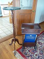 Photo shows a marble roped stand with a round top and spindle turned wood column, next to a smaller dark wood stand with a drawer and book holder containing an encyclopedia.