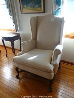 Front angle view of beige wingback armchair showing rolled arms, padded seat, and cabriole wooden legs.