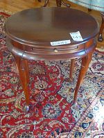 Front view of round wooden side table showing top surface, drawer, and legs.