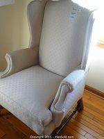 Full view of the cream wingback armchair showing upholstery, winged back, rolled armrest and cushioned seat. A label with lot number visible on backrest.