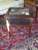 Front view of wooden display stand with glass top and glass side panels on a patterned carpet.