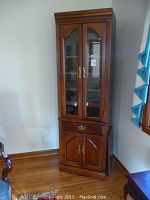 Frontal image of the tall wooden curio cabinet showing glass upper doors, single drawer, and lower doors.