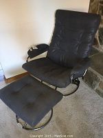 Photo showing black leatherette cushioned chair with chrome metal frame and matching ottoman on carpeted floor.