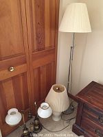 Photo showing four lamps together: two matching brass and glass table lamps, a tall metal floor lamp with white pleated shade, and a smaller white table lamp with pleated shade.