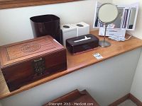 Wide shot showing the wooden jewelry box, bathroom accessories including waste bin, tissue box, white containers, and Jerdon lighted vanity mirror on a wooden shelf.