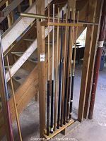 Wooden wall-mounted cue rack holding multiple pool cues
