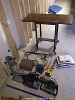 Full view of lot including small rolling table, palm sanders, Logan mat cutter, some hand tools, books and more.