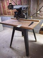 Frontal view of radial arm saw mounted on steel stand with plywood tabletop
