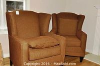 Two matching brown upholstered wingback chairs with matching pillows shown in room corner by window and fireplace.