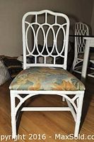 Front view of one white rattan and wicker chair with pastel floral upholstered seat on wooden floor.