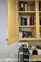 Open kitchen cabinet with insulated travel mugs, water bottles, and boxed thermal air pot