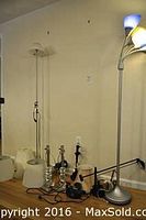 Photo showing two tall floor lamps and several table lamps with various lamp shades on the floor near a wall.