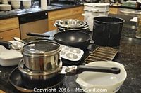 Overall view of the kitchen countertop holding the full set of pots, pans, muffin tins, ceramic bakeware, and mixing bowls arranged for display.