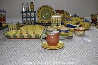Wide angle of Pfaltzgraff Pistoulet pieces arranged on carpet, showing multiple serving trays, plates, bowls, candleholders, and other serve ware in yellow, green, blue, and rust folk art style pottery.