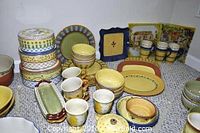 Photo showing assortment of ceramic serving ware including mugs, plates, bowls, and platters in Pistoulet design with colorful hand-painted motifs.
